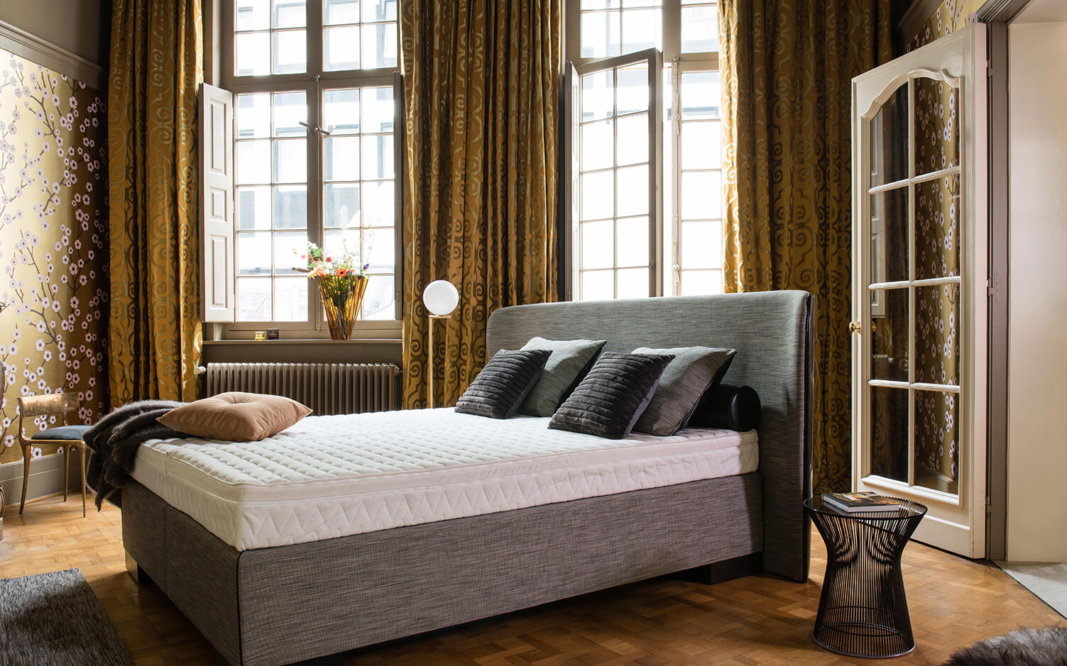 Wasserbett in Boxspring-Optik in einem Altbauzimmer mit hohen Fenstern