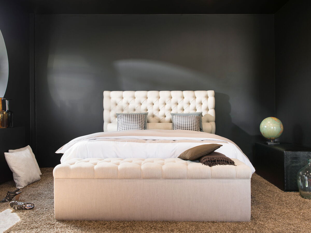 Cremefarbenes Boxspringbett im Showroom vor dunkler Wand