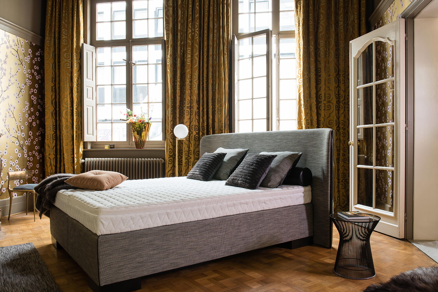 Wasserbett in Boxspring-Optik in einem Altbauzimmer mit hohen Fenstern